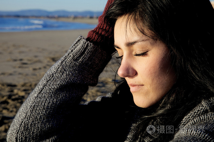 闭着眼睛感觉疼痛在海滩上的伤心女人