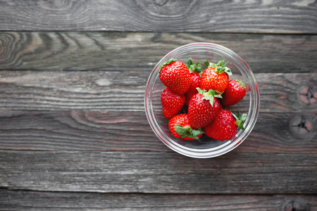 在玻璃碗里新鲜多汁的草莓。质朴的木制背景。顶视图，为文本位置