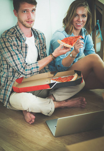 对年轻的夫妇有披萨午餐后搬入新屋与他们周围的盒子在地板上打破。对年轻的夫妇