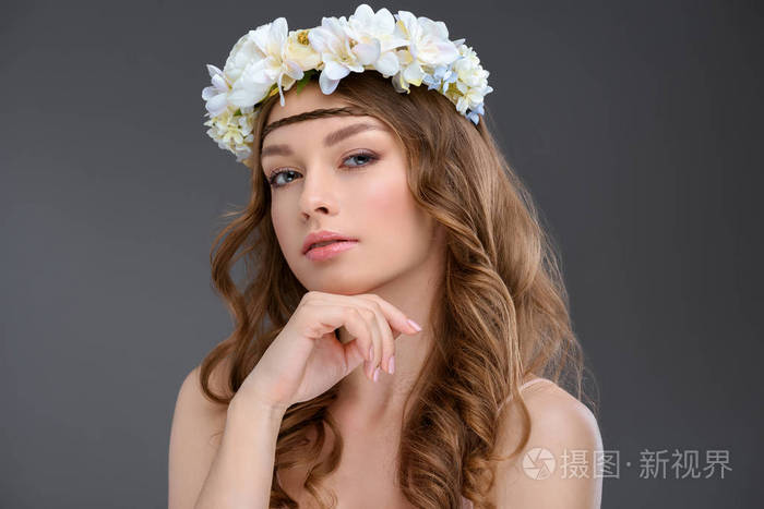 有吸引力的年轻妇女与卷曲的头发在花花圈在灰色隔绝了