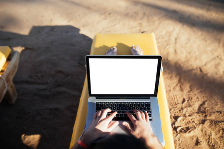 在海边的背景下, 用白色的屏幕在笔记本电脑上的年轻人的打字手关闭