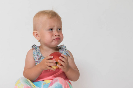 生气的蹒跚学步的女孩坐，抱着红红的苹果