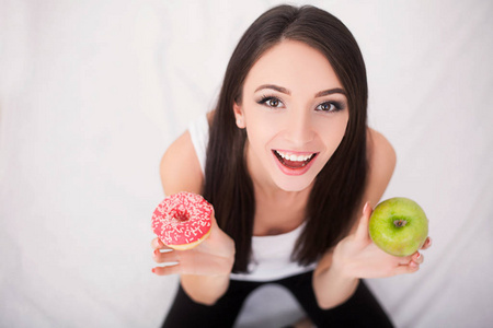 节食的概念。年轻女子水果和糖果之间选择