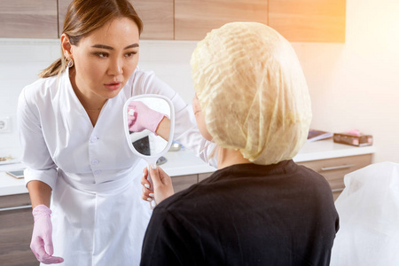 黑发妇女医生美容师显示妇女美容程序的结果在医疗办公室