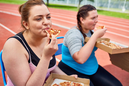 饥饿的大女性在体育场运动后吃比萨饼
