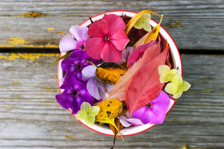 五颜六色的树叶和花朵旧木桌上的陶瓷碗里