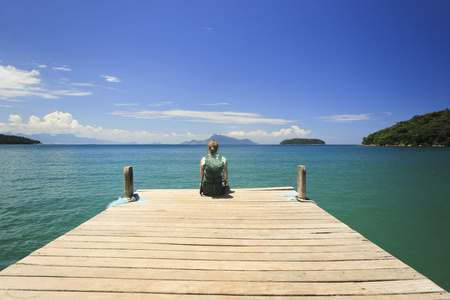 旅行者坐在码头在海洋海滩与绿水