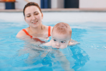 白种白人母亲训练她的新生婴儿在游泳池里漂浮。婴儿在水中潜水。健康积极的生活方式。家庭活动与早期发展观