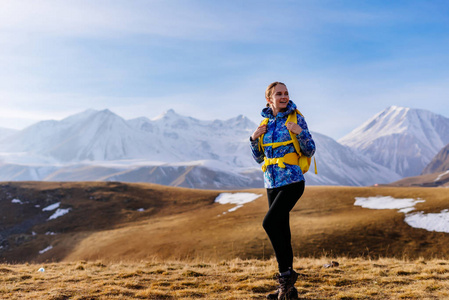 穿着蓝色夹克的年轻活泼的女孩带着背包沿着高加索山脊旅行