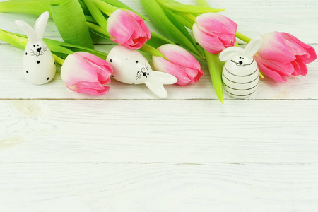 复活节兔子和一束粉红色的郁金香在白色的木制背景。复制空间