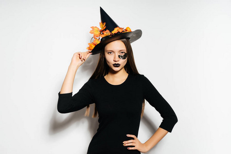 一名年轻的哥特式女孩庆祝万圣节女巫，大的黑色帽子，装饰着黄色秋天的落叶，在图像中看上去自信