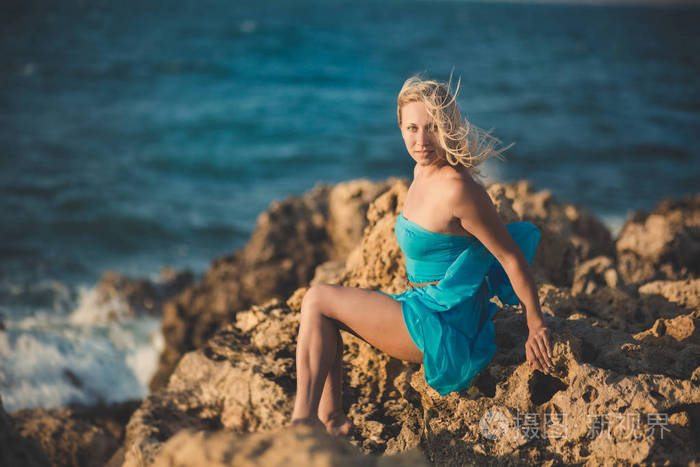 诱人的金发碧眼的女人的的双腿肩和手臂穿浅蓝色敞开的礼服在海边海边享受度假的时光孤独寂寞