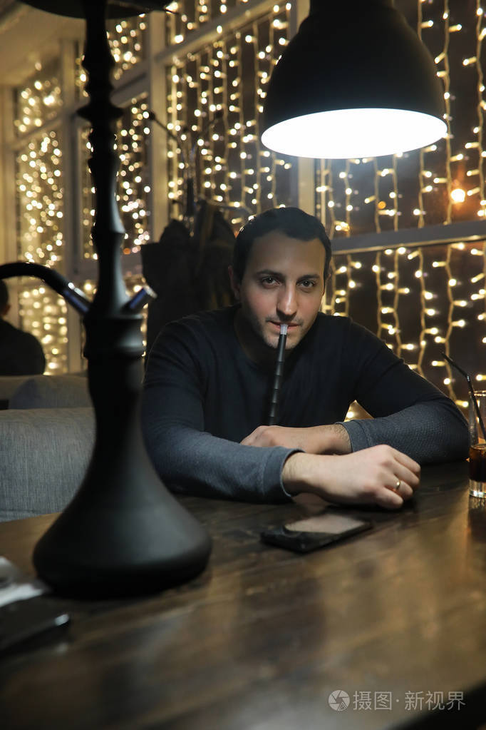 男人吸烟管的水烟中夜间咖啡馆