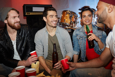 一群微笑的年轻人在地下夜总会享受聚会和喝啤酒坐在台上