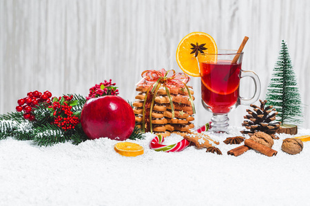 在餐桌上用肉桂棒, 圣诞树, 雪, 姜饼, 圆锥, 糖果, 新年装饰在白色的木制背景上的圣诞玻璃红酒。自由空间