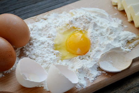 白面粉用鸡蛋 黄油和木勺烹饪板上
