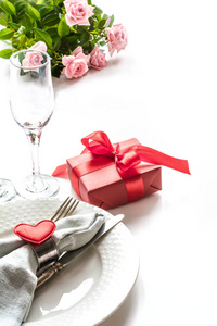 情人节晚餐与桌地方设置与红色礼物, 玻璃为香槟, 心脏装饰品与银器在白色。关门了情人卡