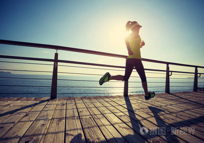 在日出时在海滨木板上奔跑的运动健身妇女