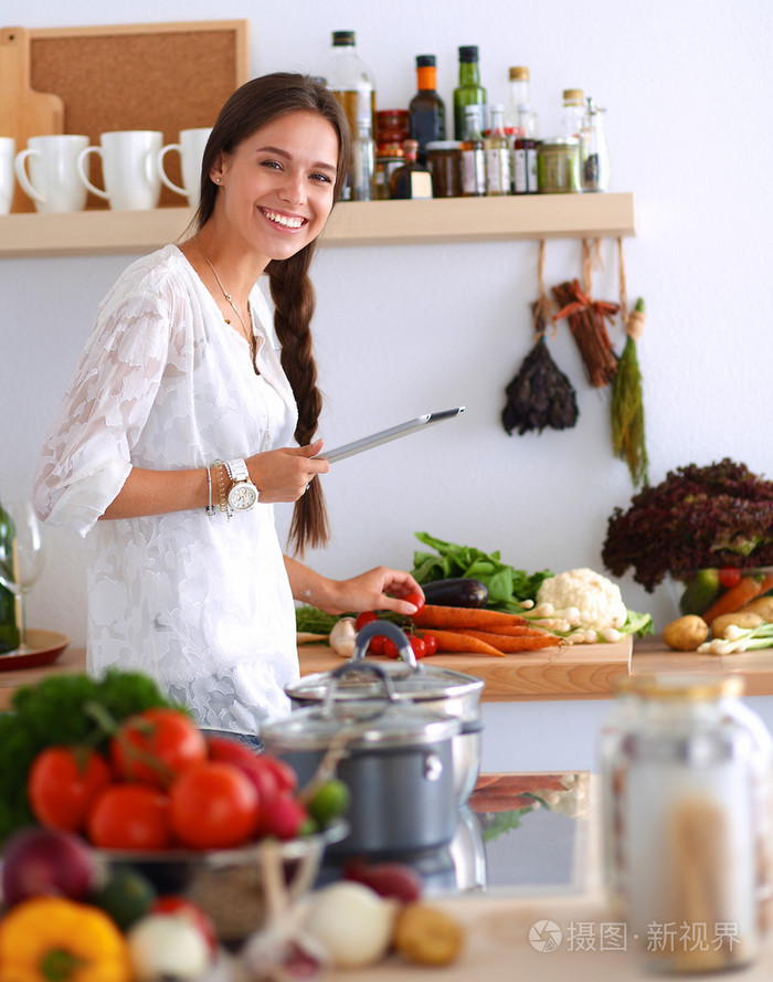 使用一台平板电脑,在她的厨房里做饭的年轻女人