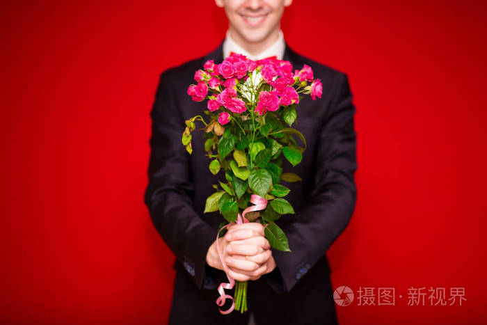 穿着西装的男士手持一束红色背景的鲜花