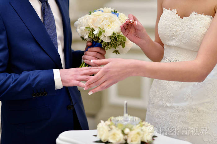 身穿美丽的新娘与英俊的新郎戒指彼此.新婚夫妇在结婚典礼上.