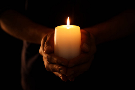 手持蜡烛在年轻人在黑暗中手持燃烧的蜡烛照片