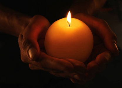 年轻人在黑暗中手持燃烧的蜡烛