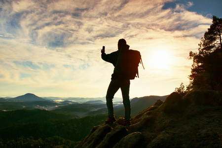 沉重的背包游客拍照智能手机。男人在岩石山峰上。梦幻般的古板的山谷