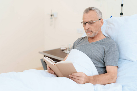 那位老人躺在医务室的小床上看书。他戴上眼镜