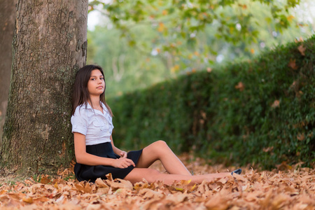 坐在秋天的树叶上的女孩