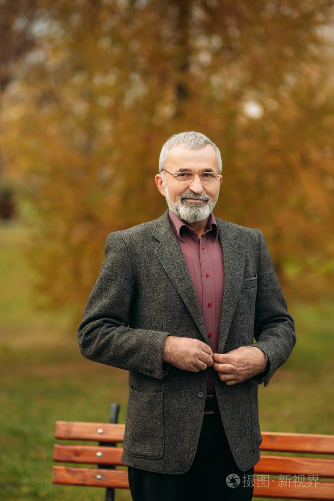 一个戴眼镜的英俊老人正在用手机.秋天在公园漫步