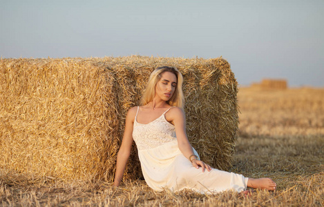 有吸引力的时髦女人在长的白色夏天衣裳在草捆附近干草