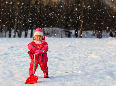 可爱的小姑娘蹒跚学步挖冬天的雪