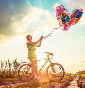 年轻女孩在的礼服骑自行车飞行空气气球