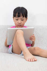 亚洲的中国小女孩坐在沙发上用平板电脑