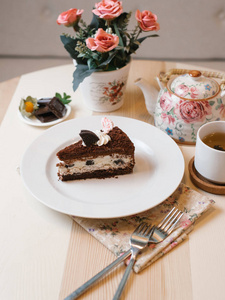 巧克力蛋糕配奶油芝士馅, 配以利奥饼干和生奶油, 配有叉子, 餐巾, 杯茶, 茶壶和花花束。
