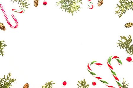 白色背景上的圣诞节组成。圣诞框架与拐杖糖 绿色崖柏树枝 松果和野生玫瑰红果。顶视图，平躺