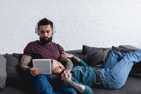 纹身女友睡觉和男朋友听音乐与平板电脑在沙发上
