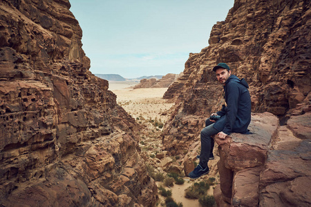 英俊的男人，穿着黑色的衣服，坐在瓦迪鲁姆沙漠中约旦的红色岩石上