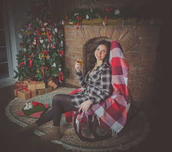 美丽的女孩在圣诞节在扶手椅与一杯红酒的格子衬衫