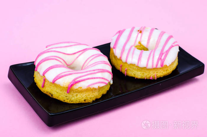 黑色盘子里的两个新鲜圆形甜甜圈