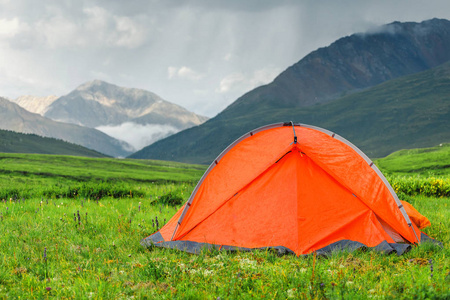一个明亮的橙色帐篷是设置在一个美丽的草坪在山上, 一个轻松的户外娱乐的概念