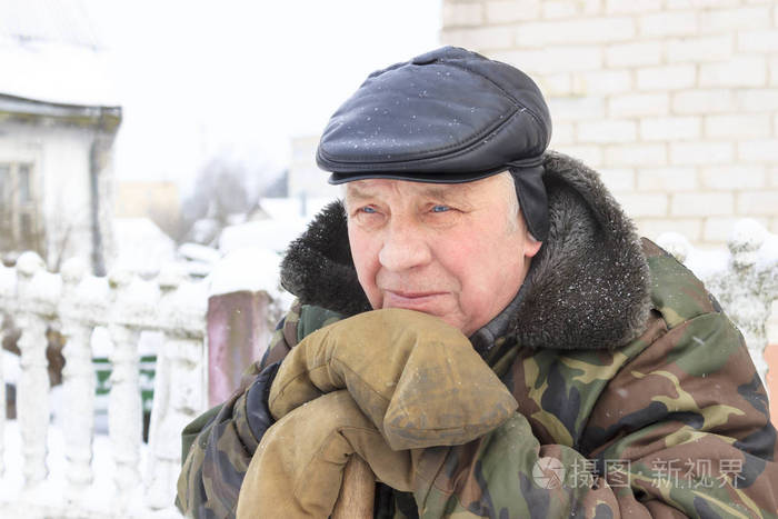 冬天冷一个老人靠在木桩上夹克是肮脏的绿色手套也是泥