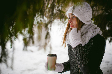 白色的围巾，帽子的可爱女人肖像针织外套上的雪的户外背景和模糊冷杉的枝条在冬天