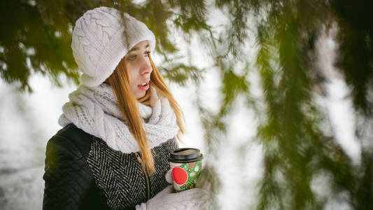 白色的围巾，帽子的可爱女人肖像针织外套上的雪的户外背景和模糊冷杉的枝条在冬天