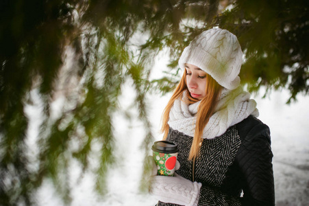白色的围巾，帽子的可爱女人肖像针织外套上的雪的户外背景和模糊冷杉的枝条在冬天
