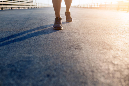 女性运动员腿部和鞋子在行动上盖路户外在日落时
