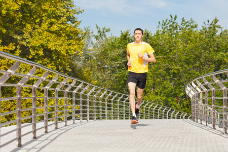 夏季在公园的城市桥梁上, 年轻的运动男子穿着履带磨损, 慢跑