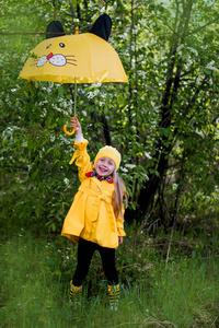 性格开朗的女孩，穿着黄色雨衣，一顶黄色的雨伞，在阳光明媚的春天的一天的黄帽子