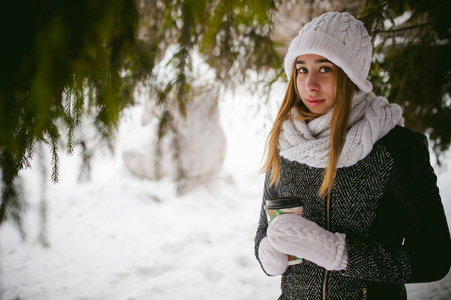 白色的围巾，帽子的可爱女人肖像针织外套上的雪的户外背景和模糊冷杉的枝条在冬天